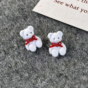 Close-up of white flocked bear stud earrings with red bows on gray knit fabric