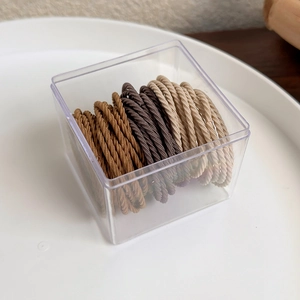 Macro detail of high-elasticity braided hair ties in various brown tones within a storage box