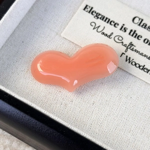 Close-up of a polished peach heart hair clip on white fabric with elegant card detail