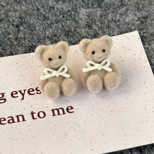 Macro shot of cute khaki flocked bear earrings with a delicate 3D white bow detail