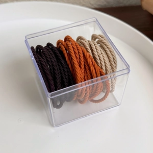 Elastic hair ties in caramel tones stored in a transparent square acrylic box