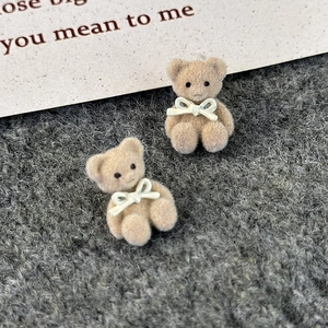 Close-up of brown flocked bear earrings with white bow detail on knit background