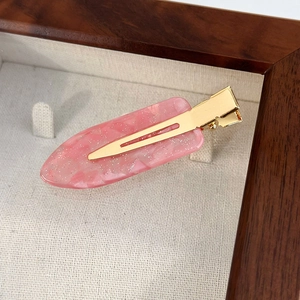 Détail d'une pince à cheveux rose en résine avec paillettes sur base en métal doré
