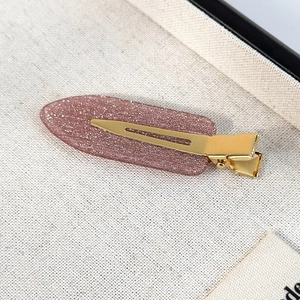 Close-up of glittery purple hair clip with gold metal duckbill clamp on textured fabric