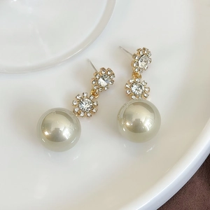 Detail of floral crystal studs and a large round pearl on elegant gold dangle earrings