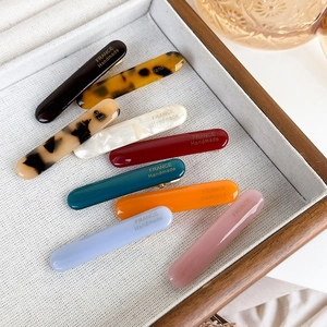 Set of 8 colorful acetate hair clips with gold logo in a minimalist wooden tray
