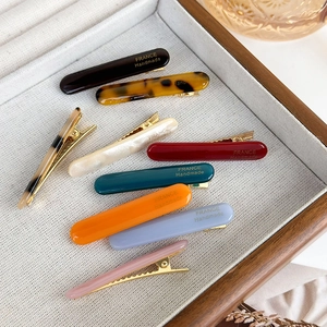 Colorful acetate barrette hair clips with gold metal base displayed on a wooden tray