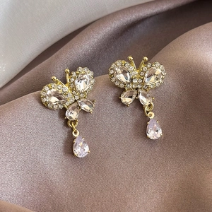 Macro shot of gold butterfly earrings with teardrop zircons on champagne satin background