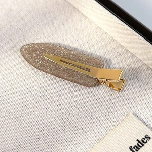Detail of champagne glitter hair clip with golden metal base on a white textured fabric