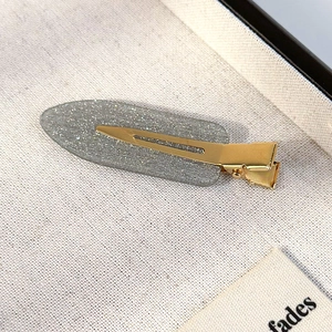 Detail view of a sparkling grey hair clip with a golden metal duckbill base for women