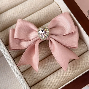Close-up of pink satin bow hair clip with a heart-shaped rhinestone in a jewelry box