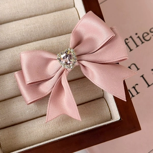 Detailed close-up of a pink satin bow clip with a sparkling heart-shaped crystal centerpiece
