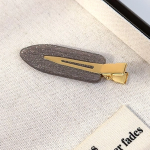 Macro shot of greyish-brown resin hair clip with silver glitter on gold metal base