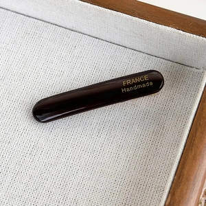 Detail of a dark tortoise acetate hair clip with golden France Handmade text on linen