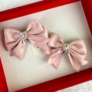 Detail view of two pink satin bow hair clips featuring crystal heart-shaped center rhinestones