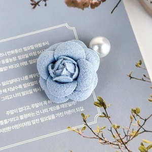 Dettaglio di un fermaglio per capelli a camelia in tessuto blu con perla bianca