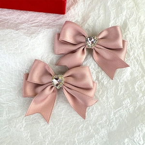 Close-up of pink ribbon hair clips with rhinestone heart detail on white textured paper