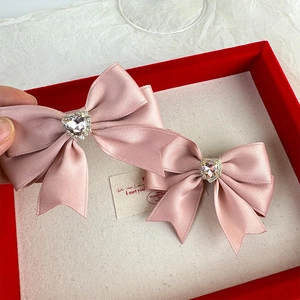 Close-up of pink satin bow hair clips with heart-shaped crystal centers in a gift box
