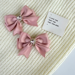 Close-up of pink satin bow hair clips with heart-shaped crystal on knit background