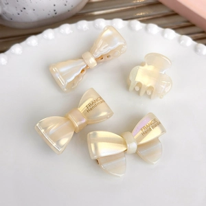 Detail of cream acetate bow hair clips and mini claw set on a white ceramic plate