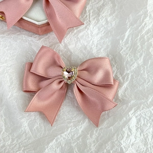 Close-up of pink satin bow hair clip with heart-shaped gemstone and crystal detail