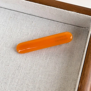 Close-up of bright orange acetate hair clip with France Handmade gold lettering detail