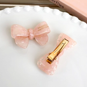 Detail view of pink marble acetate bow hair clips with gold metal duckbill clips