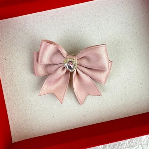 Close-up of pink satin bow hair clip with crystal heart detail in a red gift box
