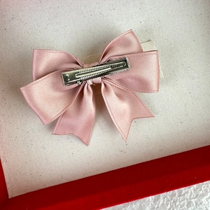 Close-up of pink satin bow hair clip with silver metal alligator clip on reverse