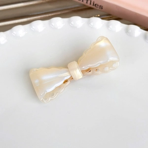 Detailed macro of cream acetate bow hair clip with pearlescent finish on a white plate