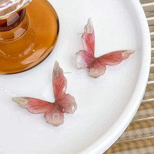 Pink gradient butterfly stud earrings with glitter details on a white ceramic plate