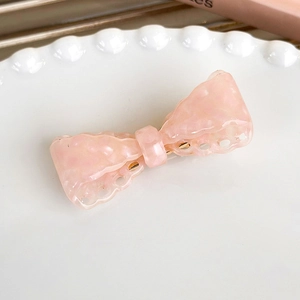 Close-up of a pink acetate bow hair clip with marble texture on a white lace plate