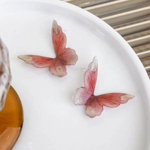 Pink gradient butterfly stud earrings with gold glitter accents on white ceramic plate