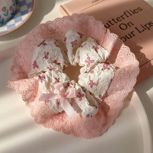 Macro detail of sweet pink bow hair scrunchie with lace trim on a white decorative tray