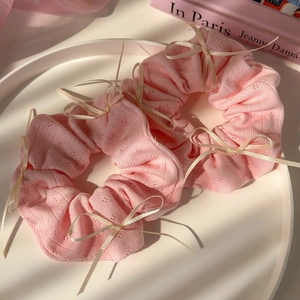 Vue détaillée de deux chouchous en tricot rose avec nœuds crème sur un plateau blanc