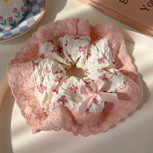 Close-up of pink lace scrunchie with bow print and ribbon detail on white tray
