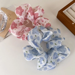 Scrunchies in chiffon floreale nei colori rosa e blu su un portagioie in legno