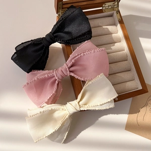 Détail des trois barrettes à nœuds en tissu superposé en noir, rose et blanc crème