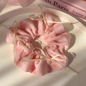 Détail d'un chouchou en maille rose avec texture losange et nœuds en satin crème