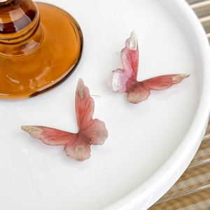 Close-up of pink gradient butterfly stud earrings with gold glitter on a ceramic tray