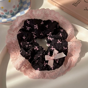 Close-up of black scrunchie with pink bow prints and lace trim on a decorative tray