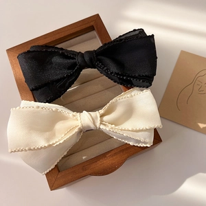 Détail de barrettes à nœuds en tissu noir et beige avec bordure perlée et texture fine