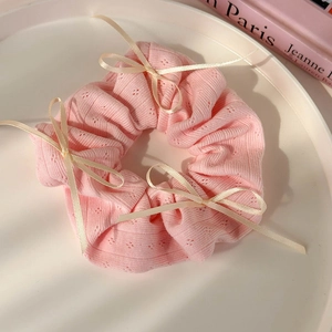 Détail d'un chouchou en tricot rose avec motifs dentelle et petits nœuds en ruban blanc