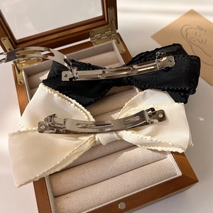 Vue détaillée de barrettes à nœuds en tissu noir et beige avec pinces en métal dans un coffret