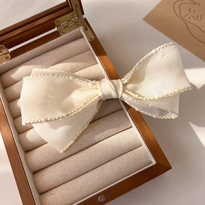 Détail d'une pince à cheveux à nœud crème avec bordure en perles sur boîte en bois
