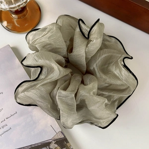 Close-up of oversized champagne chiffon scrunchie with black edge and soft pleats