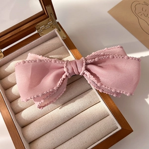 Détail d'une pince à cheveux à triple nœud en tissu rose clair avec des bords ondulés