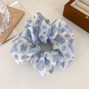 Dettaglio di scrunchie floreale in chiffon con motivi di fiori blu e bianchi
