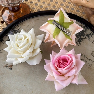 Close-up of artificial rose hair clips in cream white and pink on a vintage tray