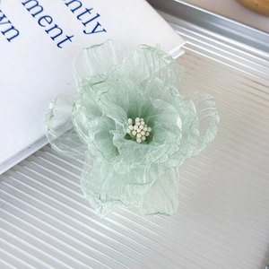 Detalle de pinza para el pelo con flor de organza verde claro y perla blanca sobre libro